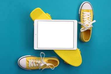 Modern tablet, kaykay ve açık mavi arka planda ayakkabılar. Metin için boşluk