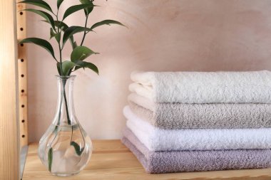 İçerideki ahşap rafta yığılmış yumuşak havlular ve yeşil yapraklar.