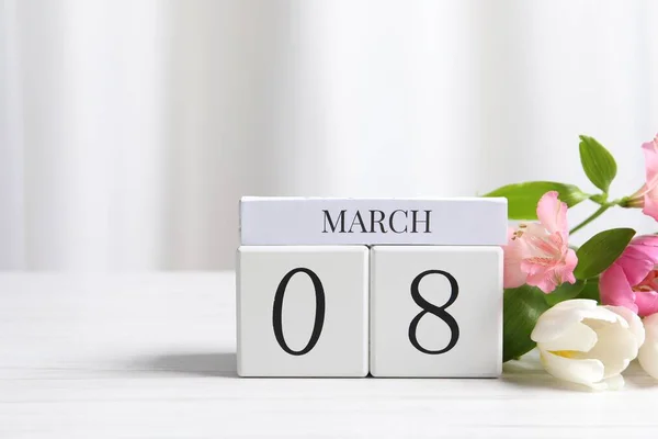International Women\'s day - 8th of March. Wooden block calendar and beautiful flowers on white table, space for text