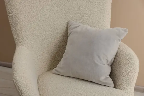 Soft grey pillow on armchair near beige wall indoors