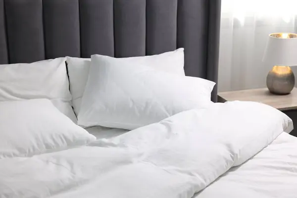 Soft white pillows and duvet on bed at home