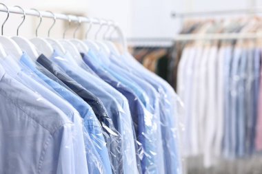 Kuru temizleme servisi. Plastik poşetlerdeki birçok farklı giysi kapalı yerlerde asılı, yakın plan.