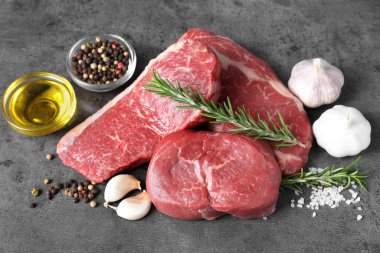 Gri masada çiğ biftek, yağ ve baharatlar.