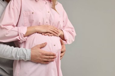 Adam açık gri arka planda hamile eşinin karnına dokunuyor, yakın plan. Metin için boşluk