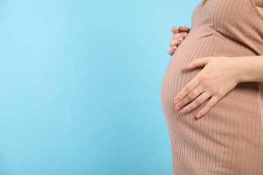 Pregnant woman on light blue background, closeup. Space for text