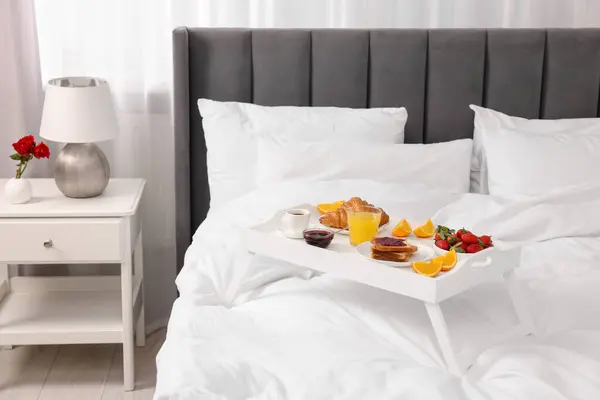 Tray with delicious breakfast on bed in room
