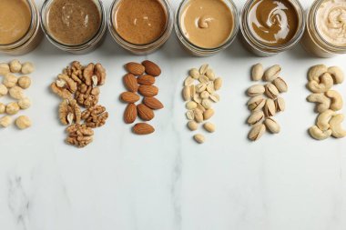 Kavanozlarda lezzetli fındık ezmesi ve beyaz mermer masada çiğ fındık. Metin için boşluk