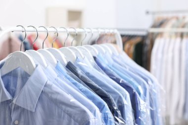 Kuru temizleme servisi. Plastik poşetlerdeki birçok farklı giysi kapalı yerlerde asılı, yakın plan.