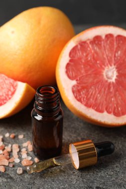 Şişede greyfurt yağı, pipet, deniz tuzu ve meyveler koyu dokulu masa, yakın çekim