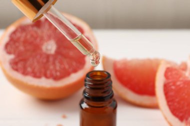 Pipetten şişeye greyfurt yağı damlıyor ve beyaz masaya taze meyve dökülüyor.