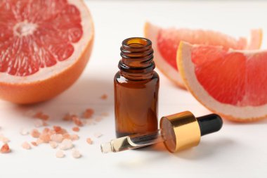 Şişede greyfurt yağı, pipet, deniz tuzu ve meyveler beyaz masada, yakın plan.