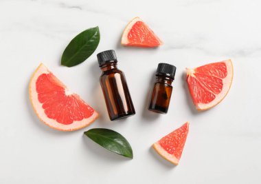 Şişelerde greyfurt yağı, yapraklar ve beyaz mermer masa üzerinde meyve kesimi, düz yatıyordu.