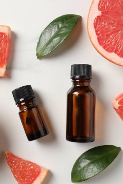 Şişelerde greyfurt yağı, yapraklar ve beyaz masa üzerinde meyve kesimi, düz uzanış