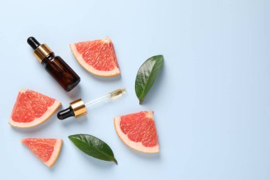 Şişede greyfurt yağı, pipet, yapraklar ve açık mavi masada meyve kesimi. Metin için boşluk