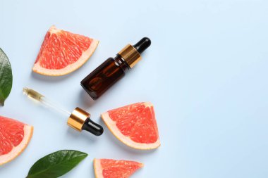 Şişede greyfurt yağı, pipet, yapraklar ve açık mavi masada meyve kesimi. Metin için boşluk