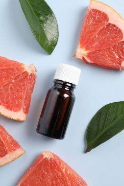Şişede greyfurt yağı, yapraklar ve açık mavi masada meyve kesimi, düz uzanma