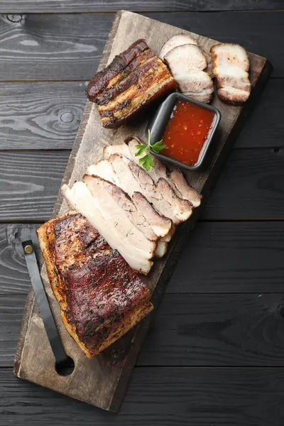 Kurutulmuş domuz eti parçaları. Sos ve maydanozla servis ediliyor. Siyah ahşap masa üzerinde.