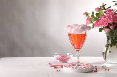 Cam kaplı pamuk helva kokteyli, marşmelov, pembe güllü vazo ve beyaz ahşap masa üzerindeki pipetler gri arkaplana karşı, metin için yer