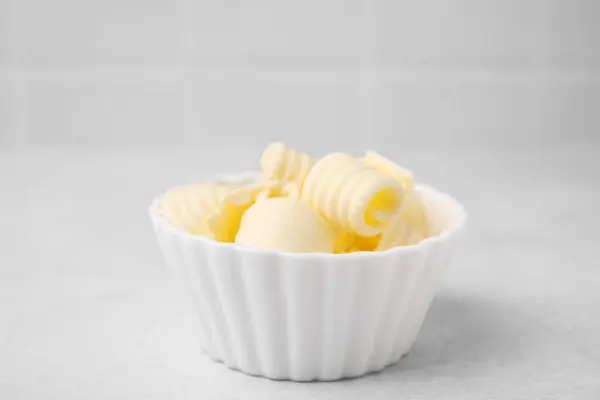 Tasty butter curls in bowl on light grey table, closeup