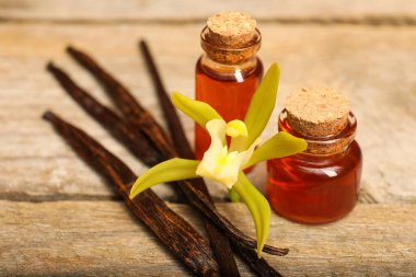 Aromatik vanilya özü, kapsüller ve çiçek ahşap masada, yakın plan.