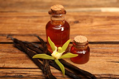 Aromatik vanilya özü, kapsüller ve çiçek ahşap masada, yakın plan.