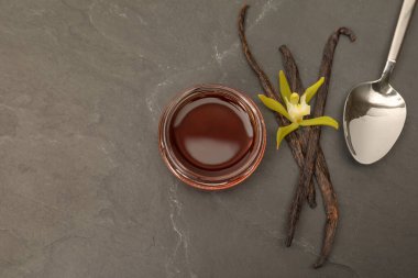 Aromatik vanilya özü, kapsüller ve çiçekler siyah masada, düz yerde. Metin için boşluk