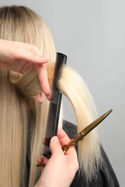 Hairdresser combing and cutting client's hair on light grey background, closeup