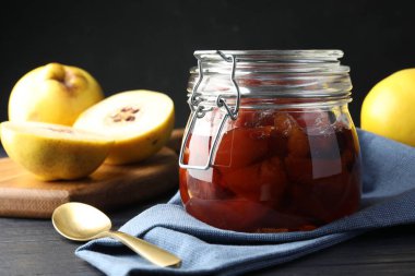 Ayva reçeli cam kavanozda, kaşık ve taze çiğ meyveler gri masada, yakın plan.