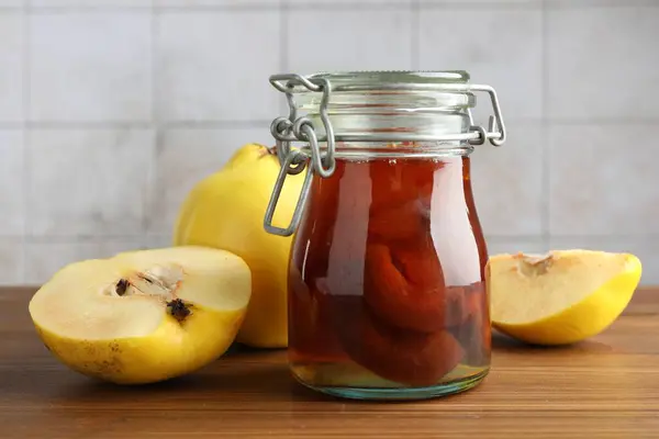Tasty homemade quince jam in jar and fruits on wooden table, closeup