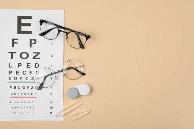 Vizyon testi çizelgesi, gözlükler, lensler ve cımbızla bej arka plan, düz yatak. Metin için boşluk