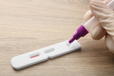 Doktor tampon çözeltisini Covid-19 ekspres test kasetine bırakıyor. Tahta masada, yakın plan.