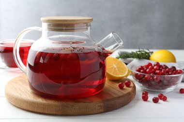 Çaydanlıkta yaban mersini çayı, beyaz ahşap masada limon ve taze böğürtlen