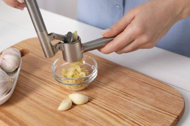 Beyaz masada basınla sarımsak sıkan kadın, yakın plan.