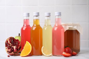 Delicious kombucha in glass bottles, jar and fresh fruits on white marble table clipart
