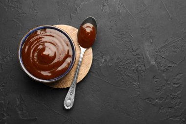 Lezzetli barbekü sosu kasede ve kaşıkla koyu dokulu masa, üst manzara. Metin için boşluk