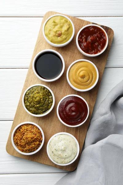 Many different sauces in bowls on white wooden table, top view