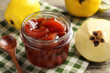 Kavanozda ev yapımı ayva reçeli, ahşap masada kaşık ve meyveler, yakın plan.