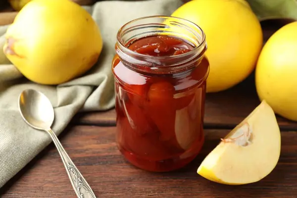 Tasty homemade quince jam in jar and fruits on wooden table