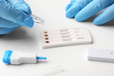 Doktor tek kullanımlık çoklu enfeksiyonlu ekspres test kasetine tampon çözeltisi bırakıyor.