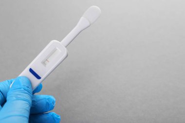 Doktor açık gri arka planda tek kullanımlık ekspres test yapıyor, yakın plan. Metin için boşluk