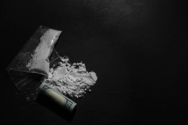 Sert uyuşturuculu plastik torba ve koyu dokulu arka planda yuvarlanmış dolar banknotu. Metin için boşluk