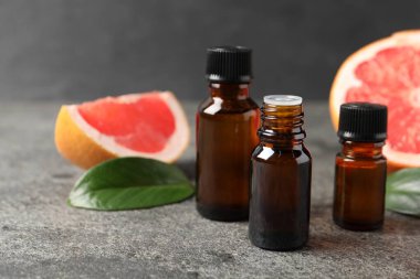 Şişelerde greyfurt yağı, yapraklar ve meyveler koyu dokulu masa üzerinde, yakın çekim