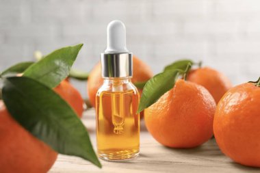 Bir şişe mandalina yağı ve beyaz ahşap masada taze meyveler, yakın plan.