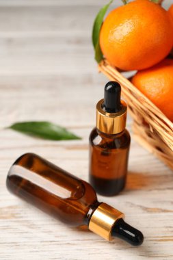 Bir şişe mandalina yağı ve beyaz ahşap masada taze meyveler.