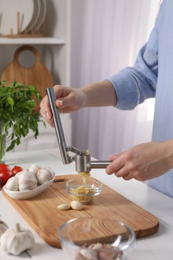 Mutfaktaki beyaz ahşap masada sarımsak sıkan kadın, yakın plan.
