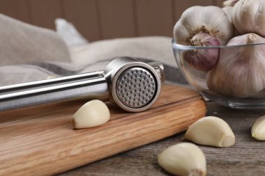 Sarımsak ezici ve karanfiller ahşap masada, yakın plan.