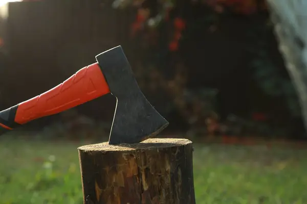 Metal axe in wooden log on backyard, closeup