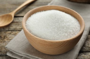 Granulated sugar in bowl on wooden table, closeup