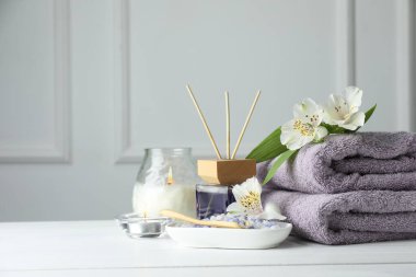 Spa kompozisyonu. Havlular, yanan mumlar, kamış oda spreyi, deniz tuzu ve beyaz ahşap masada güzel çiçekler, yazı için yer.