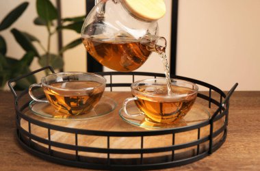 Ahşap masada cam fincana lezzetli çay dökmek, yakın çekim.